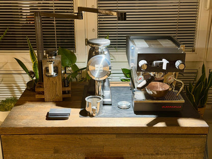 Nahaufnahme eines Espresso-Setups mit Maschine, Mühle und Zubehör auf dem Barista-Sideboard